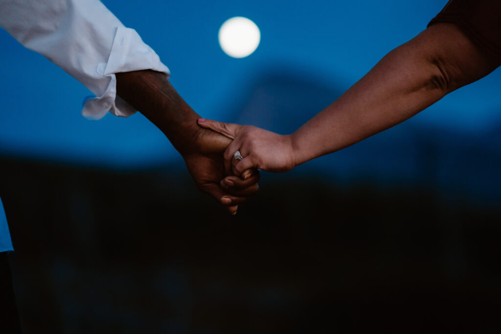 Engaged couple holds hands under the east glacier moon.